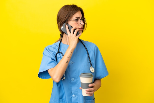 Femme médecin chirurgien isolée sur fond jaune tenant du café à emporter et un mobile