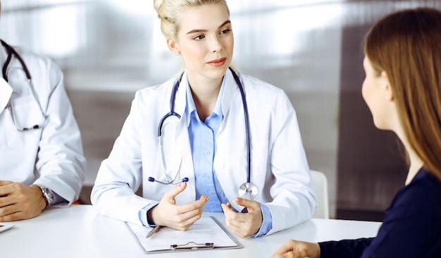 Une femme médecin avec un collègue masculin consulte une patiente assise au bureau dans une clinique moderne. Service médical parfait, concept de médecine