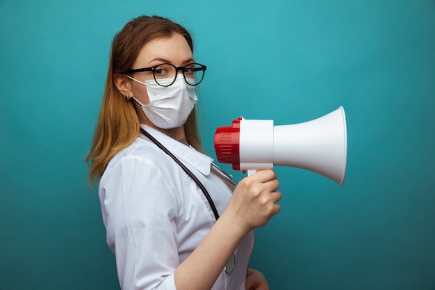 Femme médecin en combinaison de protection et lunettes avec masque tient un mégaphone.