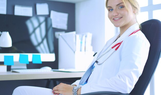 Femme médecin confiante assise au bureau et souriant à la caméra