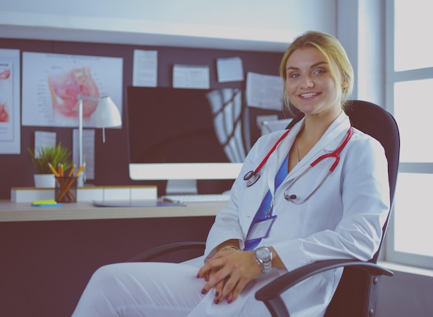 Femme médecin confiante assise au bureau et souriant à la caméra