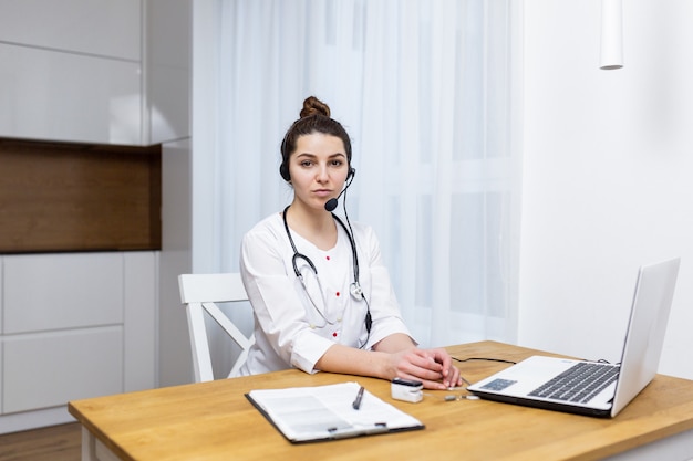 Une femme médecin consulte en ligne à l'aide d'un ordinateur portable portant des vêtements médicaux