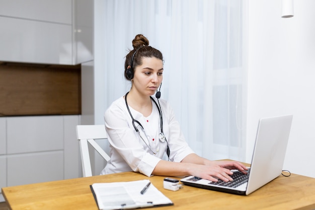 Une femme médecin consulte en ligne à l'aide d'un ordinateur portable portant des vêtements médicaux