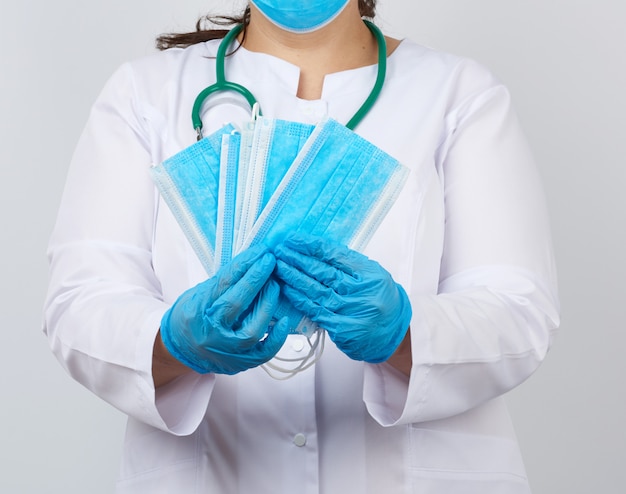 Femme médecin dans une blouse blanche et un masque détient une pile de masques protecteurs sur le virus