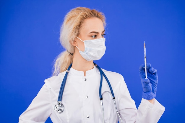 Une femme médecin dans un masque de protection avec une seringue sur fond bleu