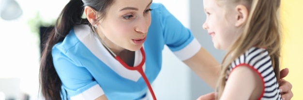 Femme médecin écoutant avec stéthoscope petite fille en clinique