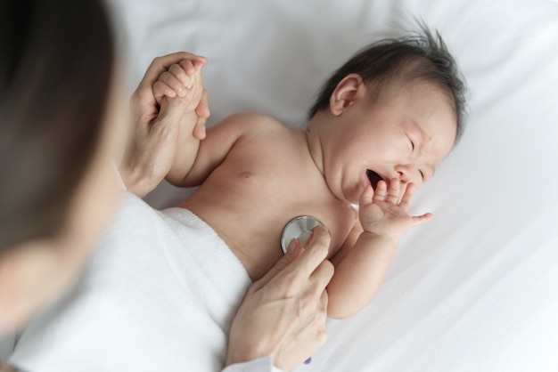 Femme médecin écoute le rythme cardiaque du nouveau-né asiatique malade qui pleure sur le lit.