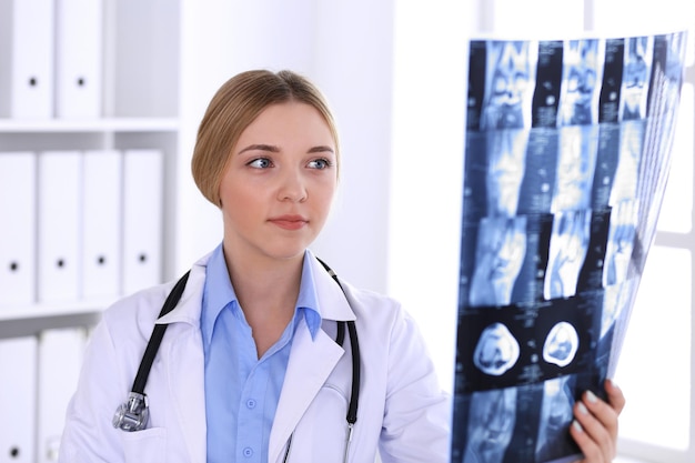 Femme médecin examinant une image radiographique près de la fenêtre à l'hôpital. Chirurgien ou orthopédiste au travail. Concept de médecine et de soins de santé. Le chemisier de couleur bleue d'un thérapeute a l'air bien.