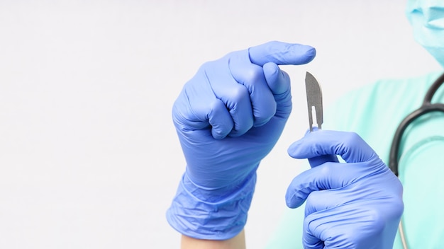 Femme médecin en gants bleus tient le scalpel à la main sur un mur blanc avec copie espace