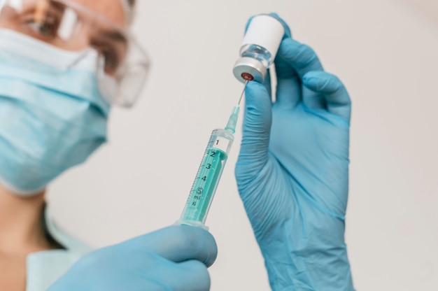 Photo femme médecin avec des gants et des lunettes de sécurité tenant un vaccin et une seringue