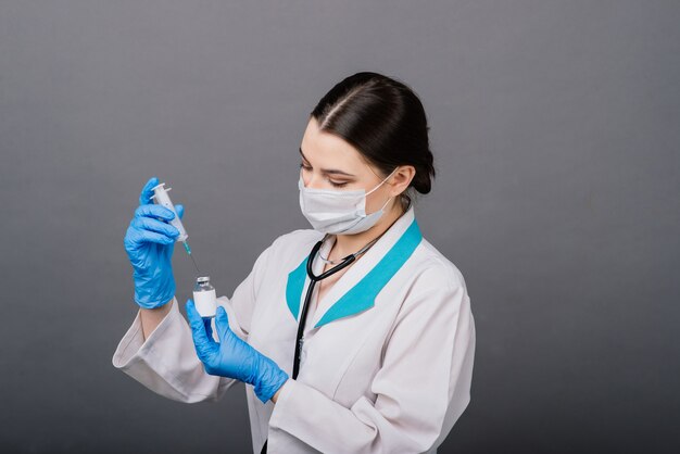 Femme médecin grave dans un masque médical tenant la seringue et le vaccin isolé sur fond gris