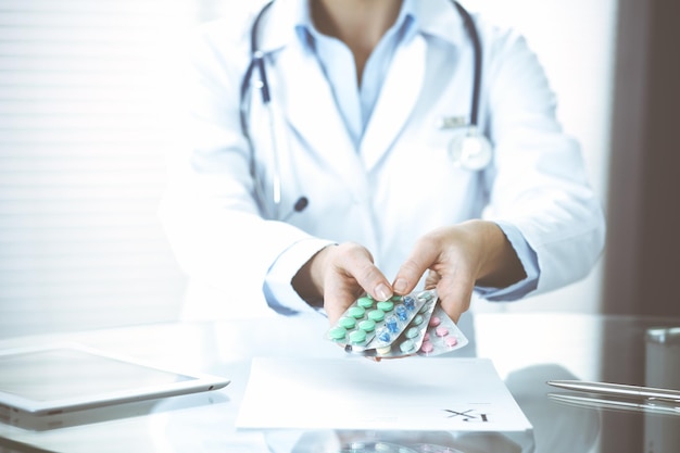 Femme médecin inconnue au travail à l'hôpital. Pilules au presse-papiers médical. Une jeune femme médecin rédige une ordonnance ou remplit un formulaire médical alors qu'elle est assise au bureau de l'hôpital, en gros plan.