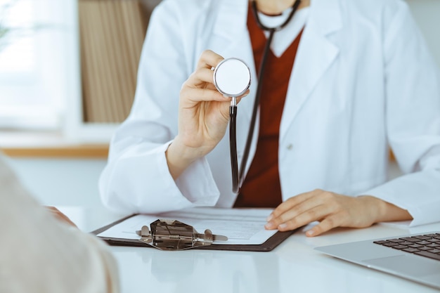 Femme-médecin inconnue avec un stéthoscope dans les mains. Le médecin est prêt à examiner un patient, gros plan des mains. Notion de médecine.