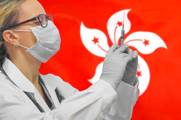 Femme médecin ou infirmière en gants tenant la seringue pour la vaccination contre le drapeau de Hong Kong