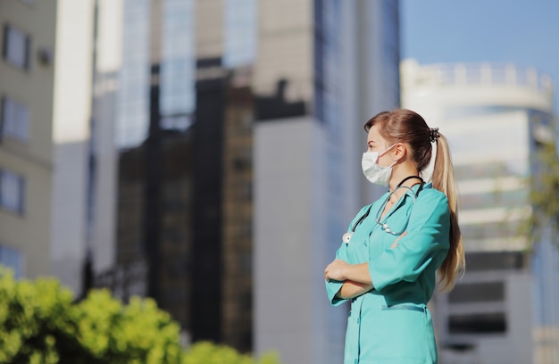 Femme médecin, infirmière portant un masque protecteur dans la ville. Gratte-ciel, ciel