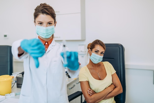 Femme médecin ou infirmière tenant un vaccin et montrant les pouces vers le bas.