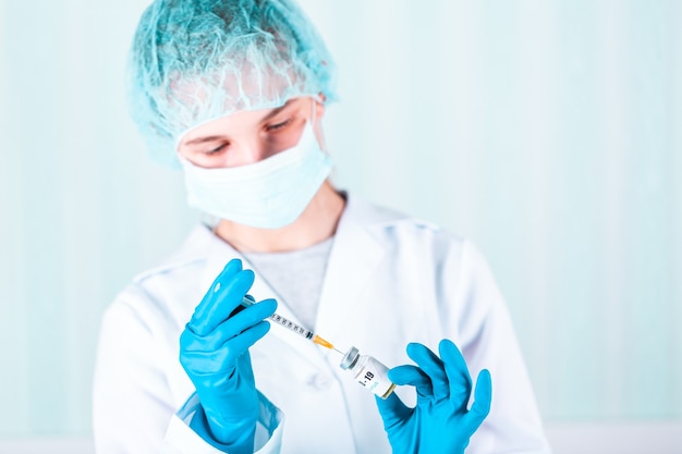 Femme médecin ou infirmière en uniforme et gants portant un masque facial de protection en laboratoire tenant une bouteille de vaccin flacon de médicament avec étiquette de vaccin COVID-19 contre le coronovirus