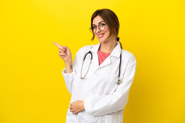 Femme médecin isolée sur fond jaune, pointant le doigt sur le côté