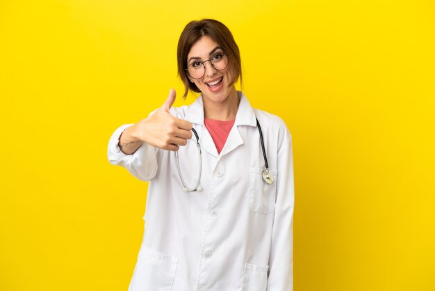 Femme médecin isolée sur fond jaune avec le pouce levé parce que quelque chose de bien s'est produit