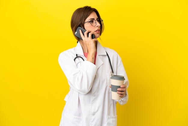 Femme médecin isolée sur fond jaune tenant du café à emporter et un mobile