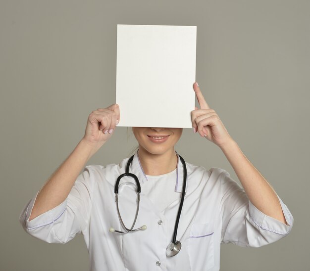 Femme médecin avec liste blanche, debout sur fond gris