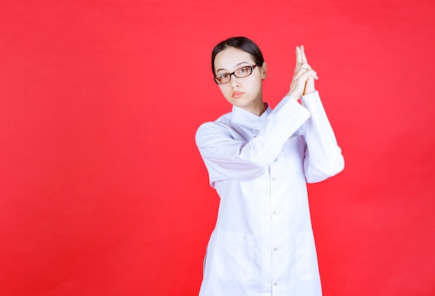 Femme médecin à lunettes debout sur fond rouge et donnant des poses neutres.