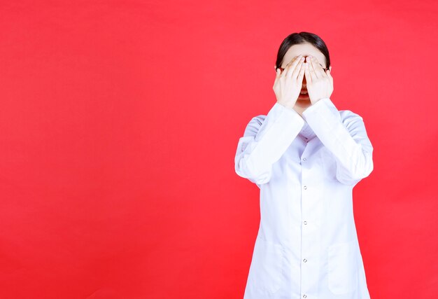 Femme médecin à lunettes debout sur fond rouge et se sentant fatigué et somnolent.