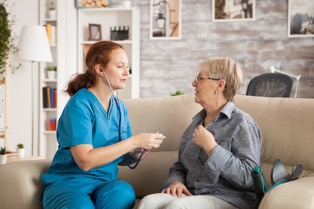 Femme médecin en maison de retraite à l'aide d'un stéthoscope pour écouter le cœur de la vieille femme.