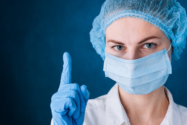 Femme médecin en masque et chapeau pointe un doigt vers le haut