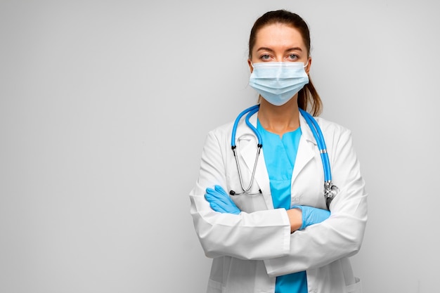 Femme médecin en masque médical debout contre le gris, portrait