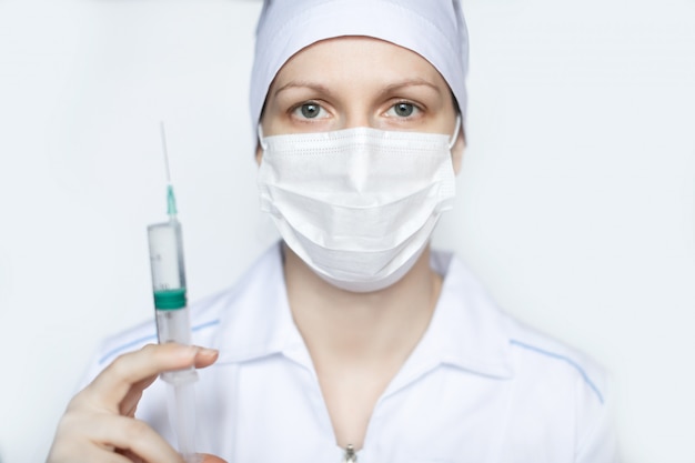 Femme médecin en masque de protection médical avec un gros plan de seringue.