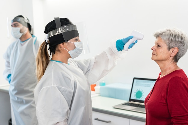 Femme Médecin Mesurant La Température D'un Patient Senior Pour Une Maladie à Coronavirus