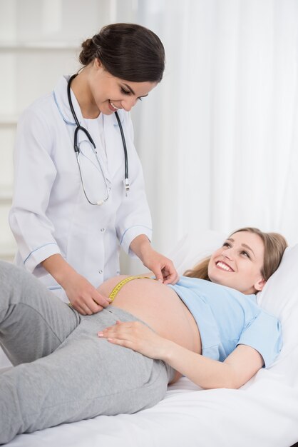 Femme médecin mesurant le ventre de sa patiente enceinte.