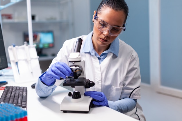 Femme médecin microbiologiste analysant les résultats des vaccins à l'aide d'un microscope médical