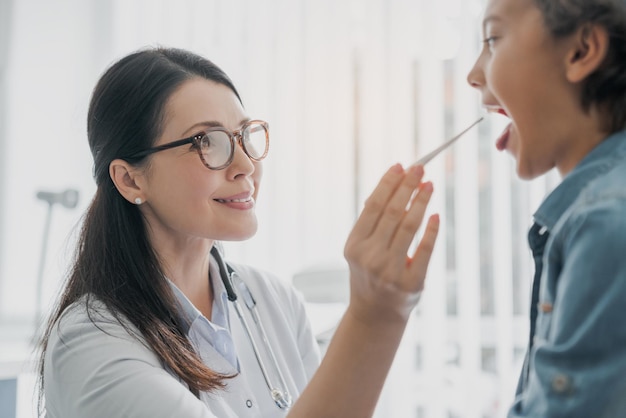 Femme médecin mixte vérifiant la bouche du garçon à la clinique