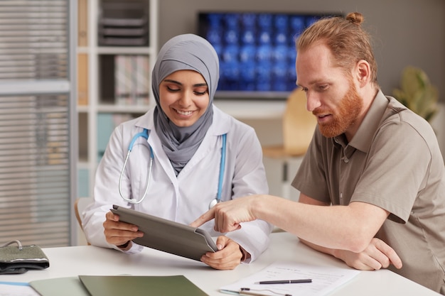 Femme médecin montrant une prescription médicale sur tablette numérique à son patient lors de sa visite à l'hôpital