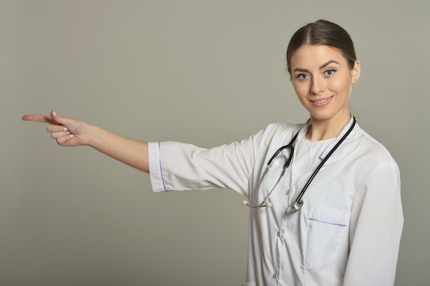 Une femme médecin montre un espace de copie vide sur fond gris