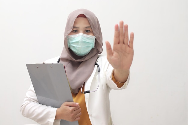 Une femme médecin musulmane debout avec un masque de protection montre l'arrêt avec un geste de la main