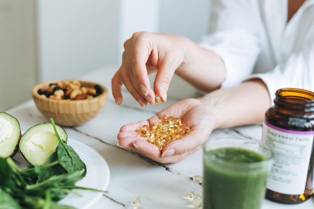 Femme médecin nutritionniste mains en chemise blanche avec des capsules de vitamine D oméga 3 avec de la nourriture végétalienne verte