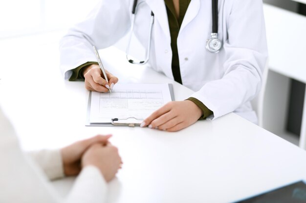 Femme Médecin Et Patient Assis Et Parlant à L'examen Médical Au Bureau De L'hôpital Agrandi