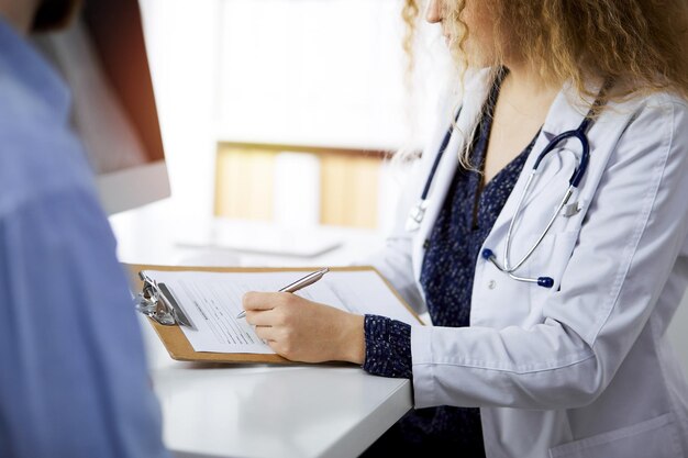 Femme médecin et patient masculin discutant de l'examen de santé actuel tout en étant assis dans une clinique ensoleillée, en gros plan. Notion de médecine.