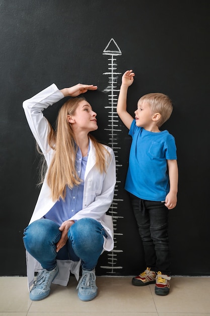 Photo femme médecin avec petit garçon mesurant la hauteur près d'un mur sombre