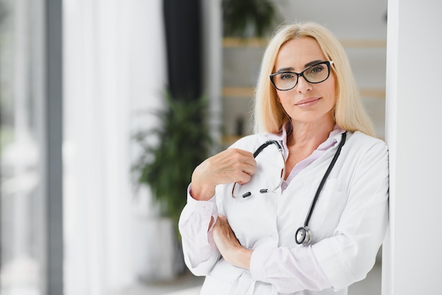 Femme médecin portant une blouse de laboratoire et un stéthoscope et tenant un presse-papiers dans ses mains tout en se tenant à l'hôpital