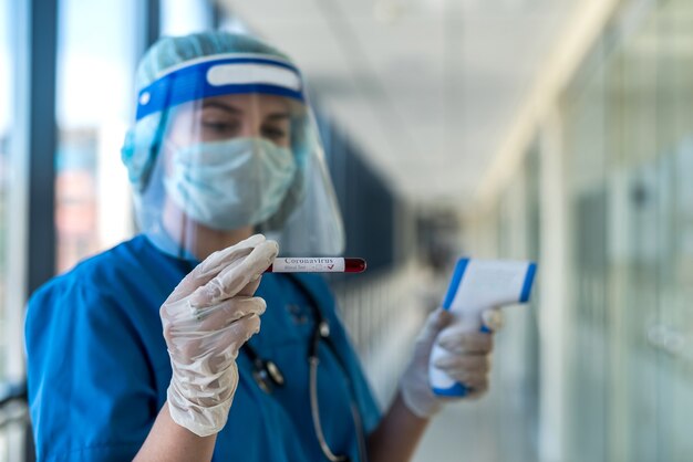 Femme médecin portant un masque de protection et un écran facial à l'aide d'un thermomètre infrarouge pour vérifier la température corporelle en clinique. covid19