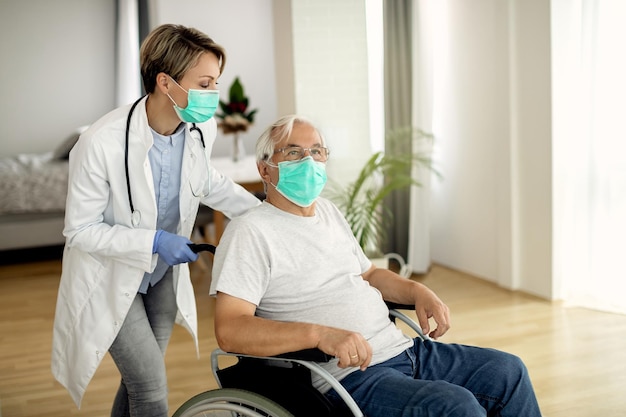 Femme médecin poussant un homme âgé en fauteuil roulant tout en lui rendant visite pendant la pandémie de COVID19