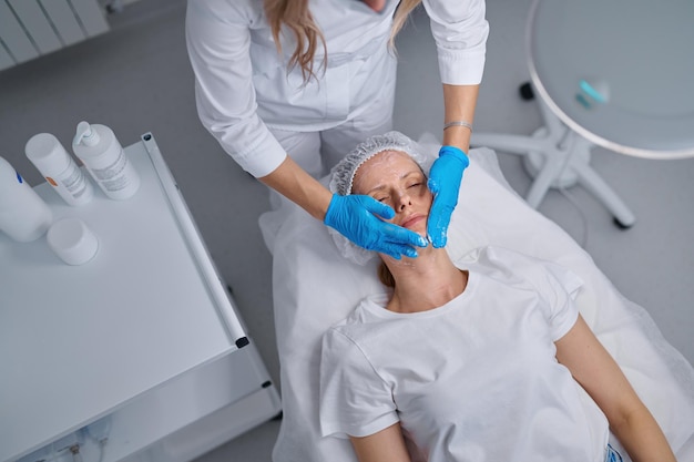 Femme médecin professionnel esthéticienne appliquant un masque sur le visage du patient pour les soins de la peau. Procédure cosmétique pour les soins de la peau, le rajeunissement et la nutrition