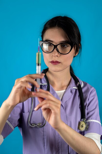 Femme médecin avec seringue posant pour appareil photo isolé sur fond de studio coloré