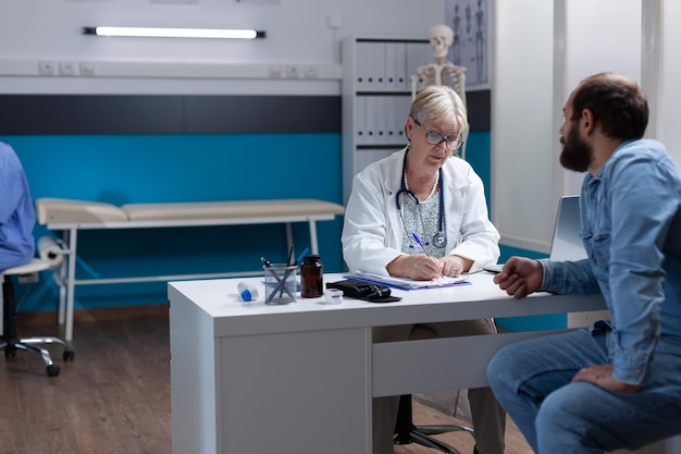 Femme médecin signant des fichiers de contrôle pour donner un traitement à l'homme après examen. Médecin écrivant des médicaments sur ordonnance et signature sur des papiers pour aider le patient lors d'un rendez-vous médical.