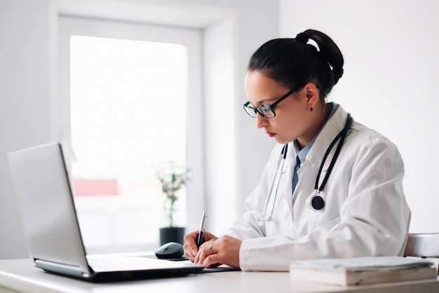 Femme médecin sur son lieu de travail avec ordinateur portable et presse-papiers