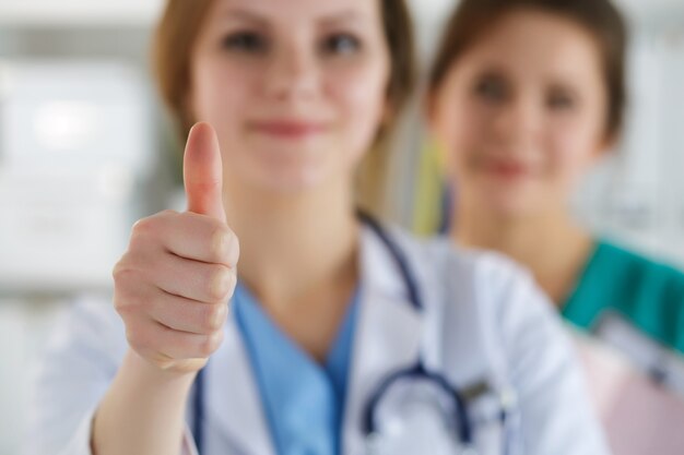 Femme médecin souriant montrant signe OK avec le pouce debout à son bureau avec son collègue